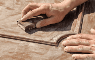 A person sanding a wooden surface with a sanding block.