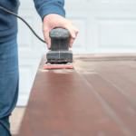 A person using an electric sander on a wooden surface.
