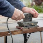 A person using an electric sander on a wooden surface.