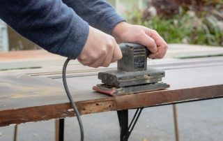 A person using an electric sander on a wooden surface.